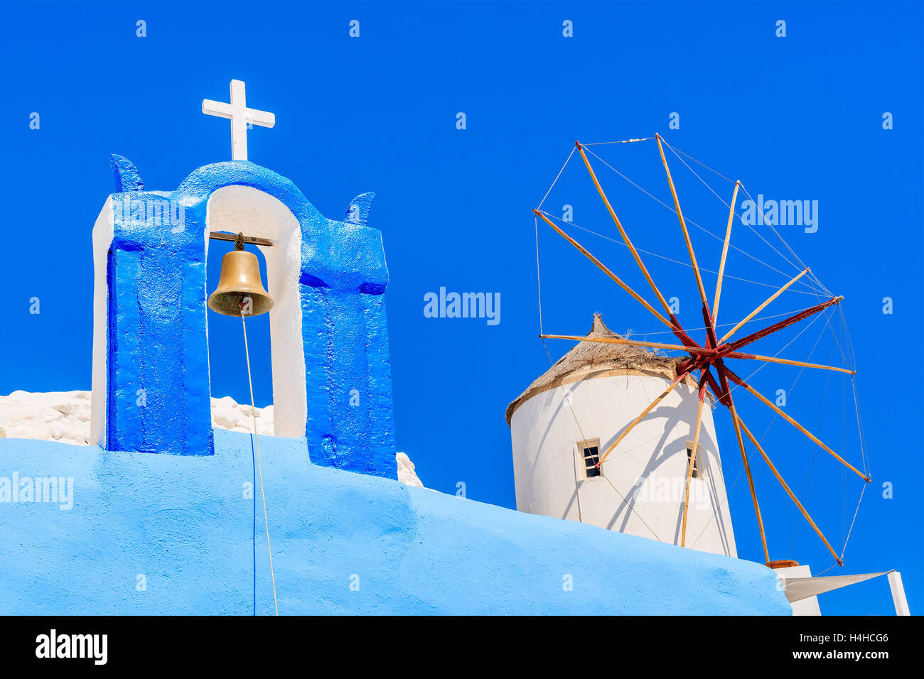 Typical Greek church tower and windmill with blue sky in background in Oia village, Santorini island, Greece Stock Photo