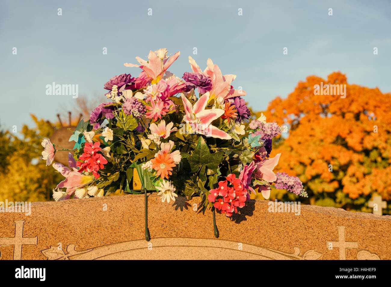 Flowers in a cemetery with large maple trees in the background, in