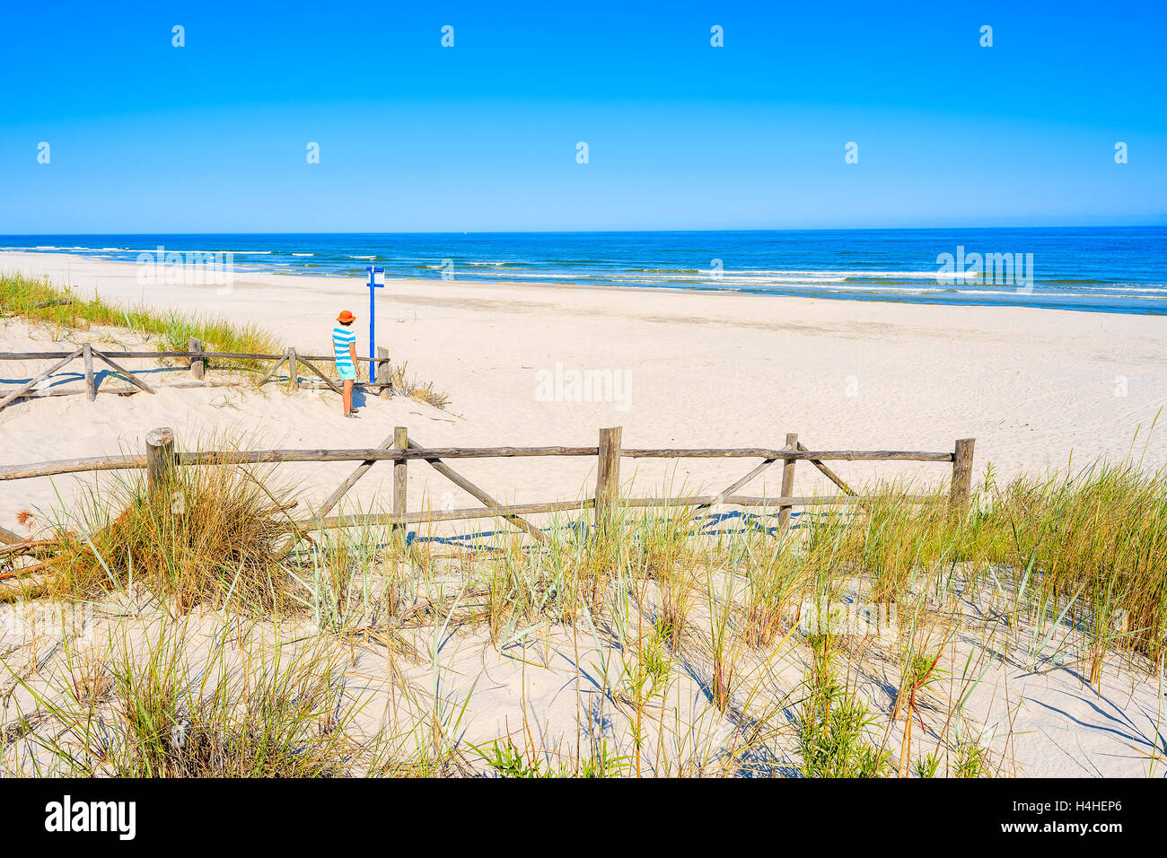 Young woman tourist standing at entrance to beautiful sandy beach in Lubiatowo coastal village, Baltic Sea, Poland Stock Photo