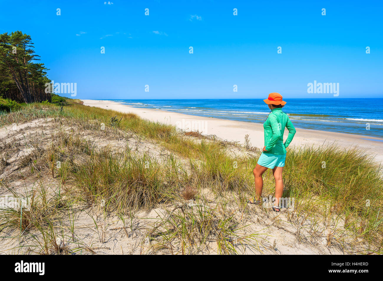 Young woman tourist standing on sand dune and looking at beautiful beach in Lubiatowo coastal village, Baltic Sea, Poland Stock Photo