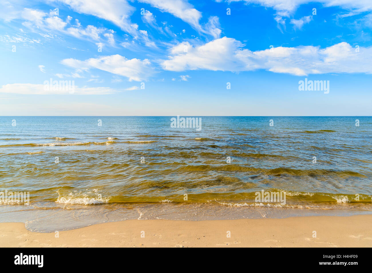 Sea waves on sandy beach and white sunny clouds on blue sky in Debki village, Baltic Sea, Poland Stock Photo