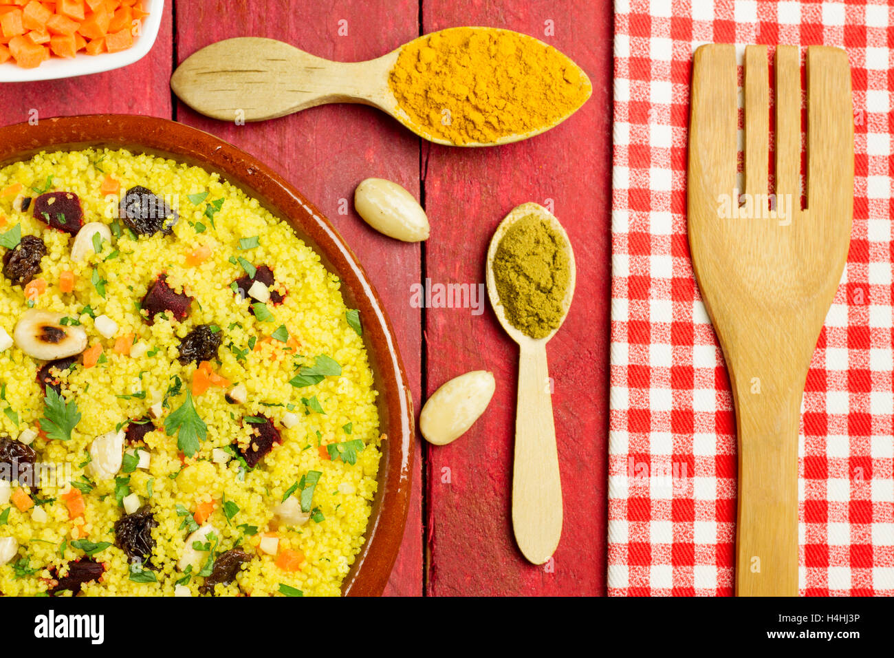 Vegetarian couscous in a clay pot, with some ingredients, spices and a wooden fork Stock Photo