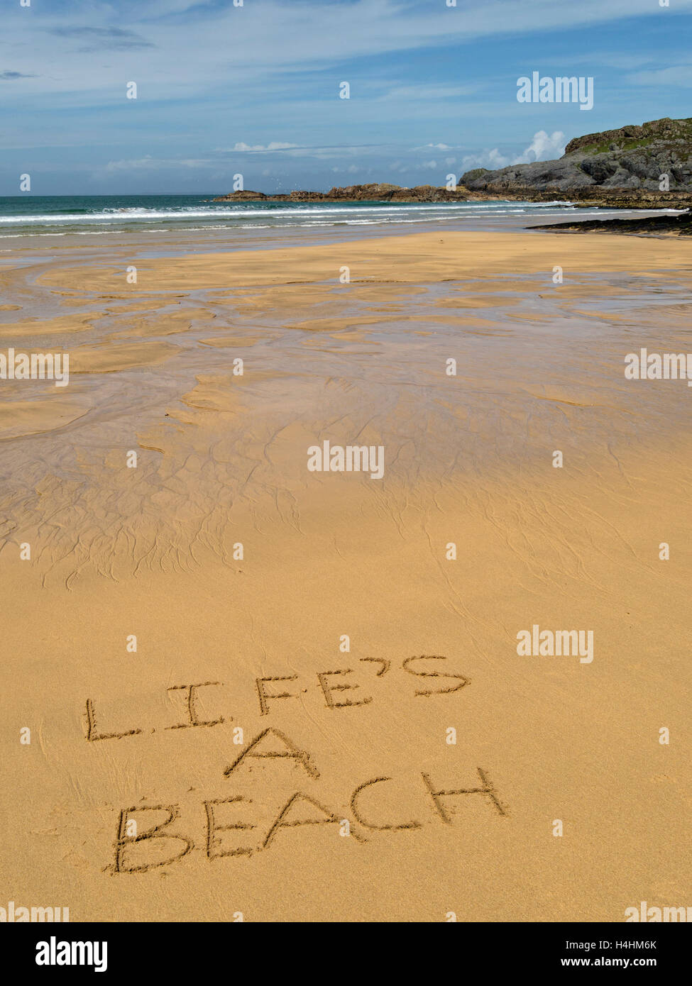 The words 'Life's a beach' written in golden yellow sand of remote Scottish beach. Stock Photo