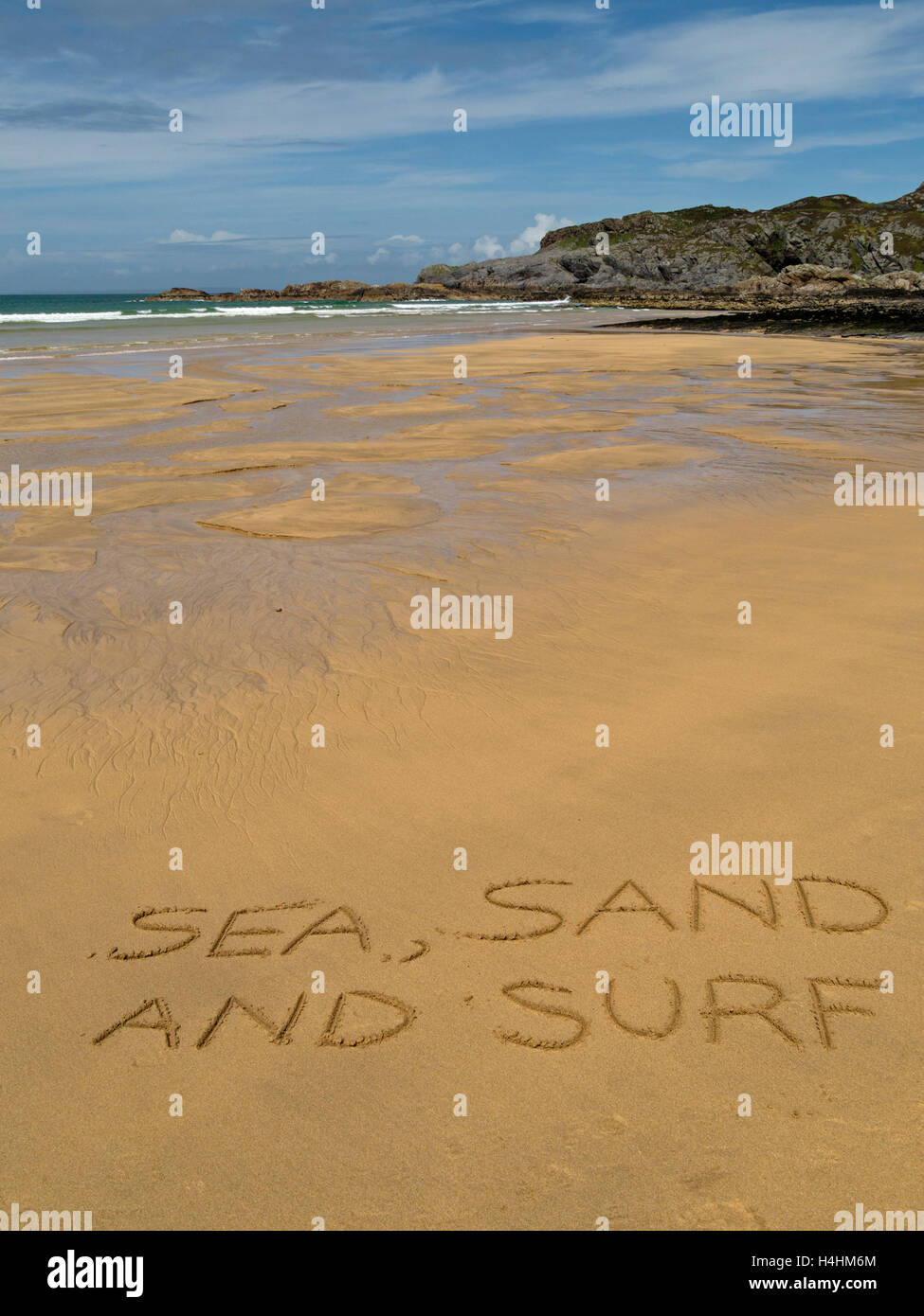 The words 'sea, sand and surf' written in golden yellow sand of remote Scottish beach. Stock Photo