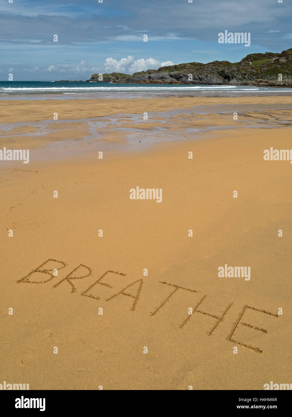 The word 'breathe' written in golden yellow sand of remote Scottish beach. Stock Photo