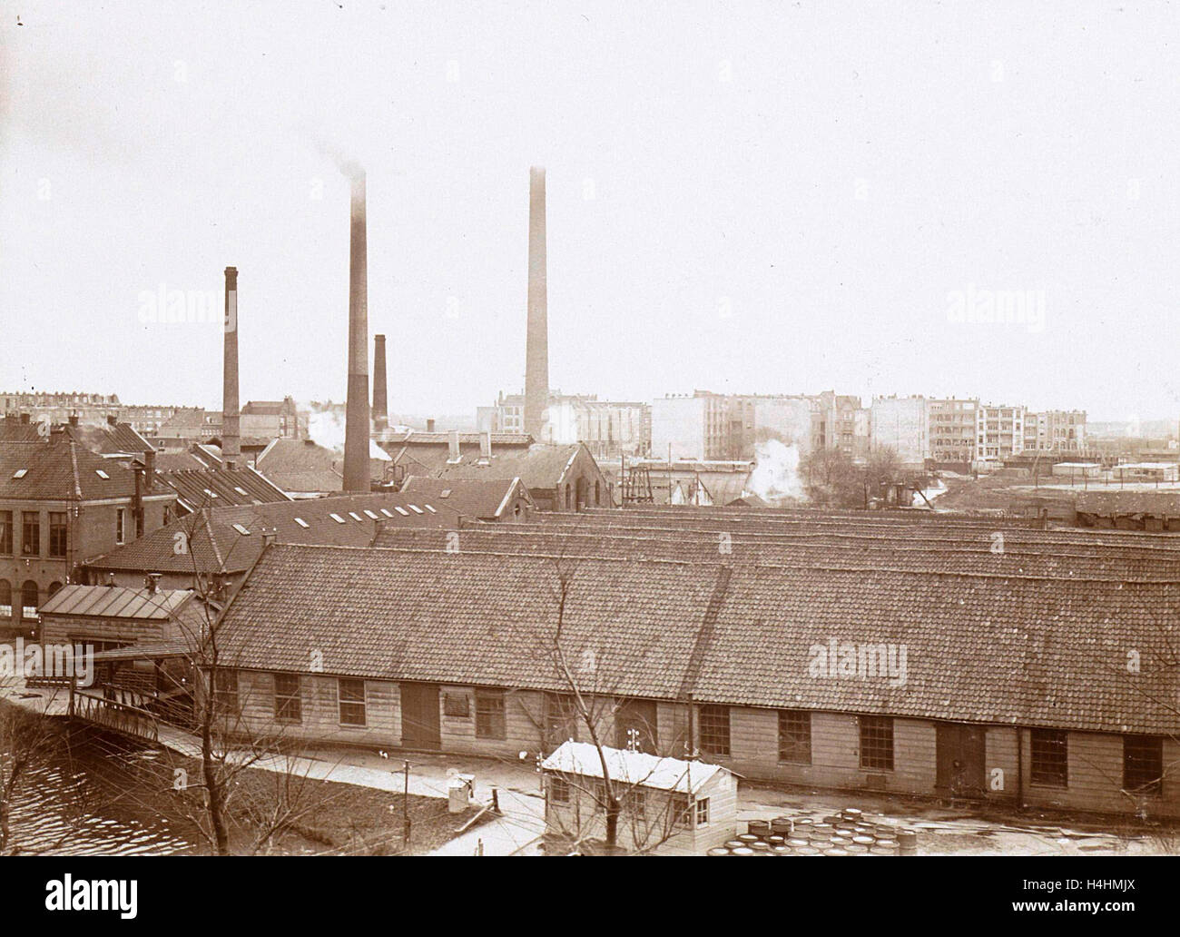 Exterior of factory buildings with chimneys, in the foreground wooden barrels, Anonymous, c. 1900 - c. 1910 Stock Photo