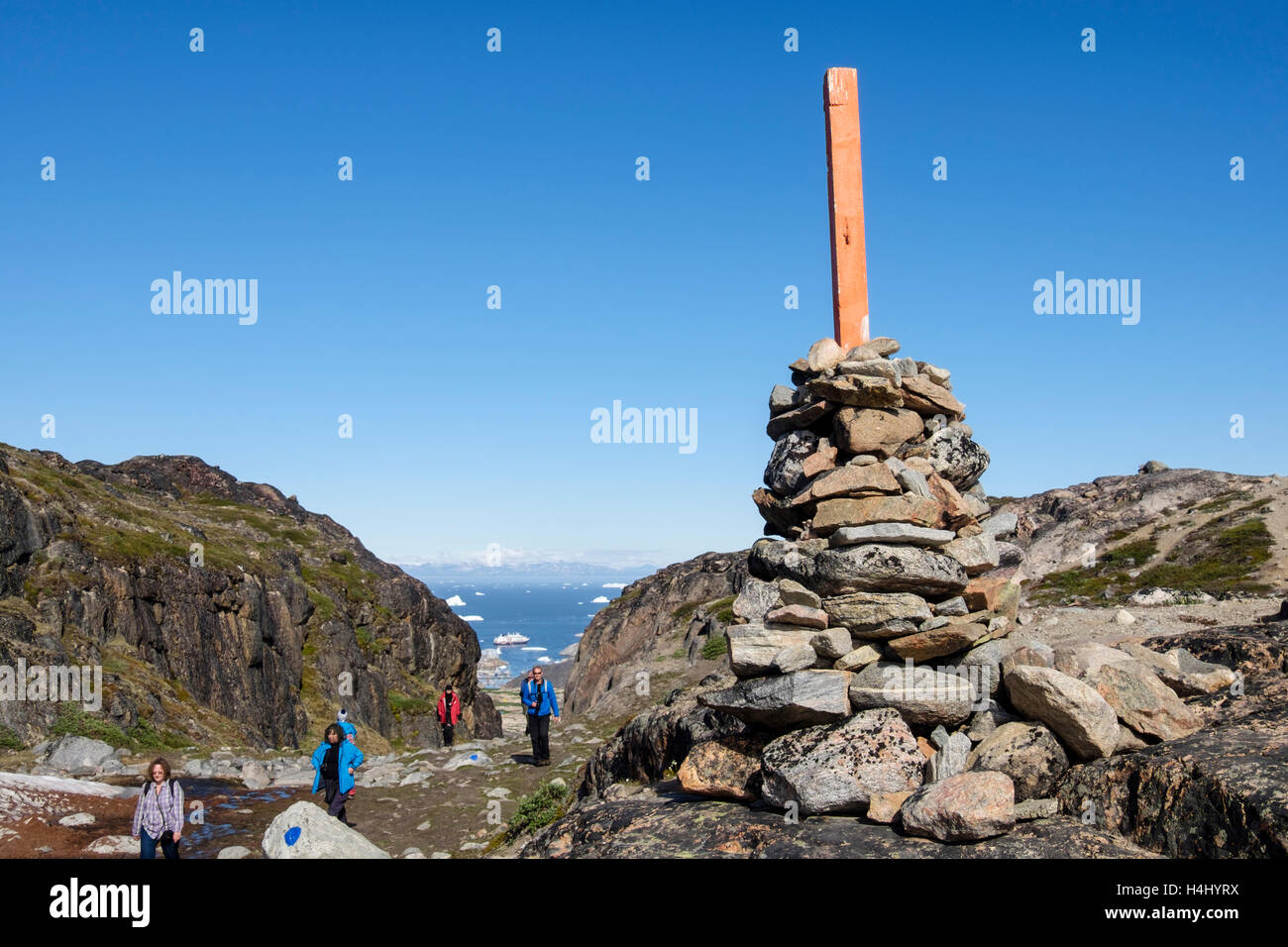 Cairn marking high point on blue route trail with people hiking to Jakobshavn Iceford and Holms Bakke in summer 2016. Ilulissat, Greenland Stock Photo