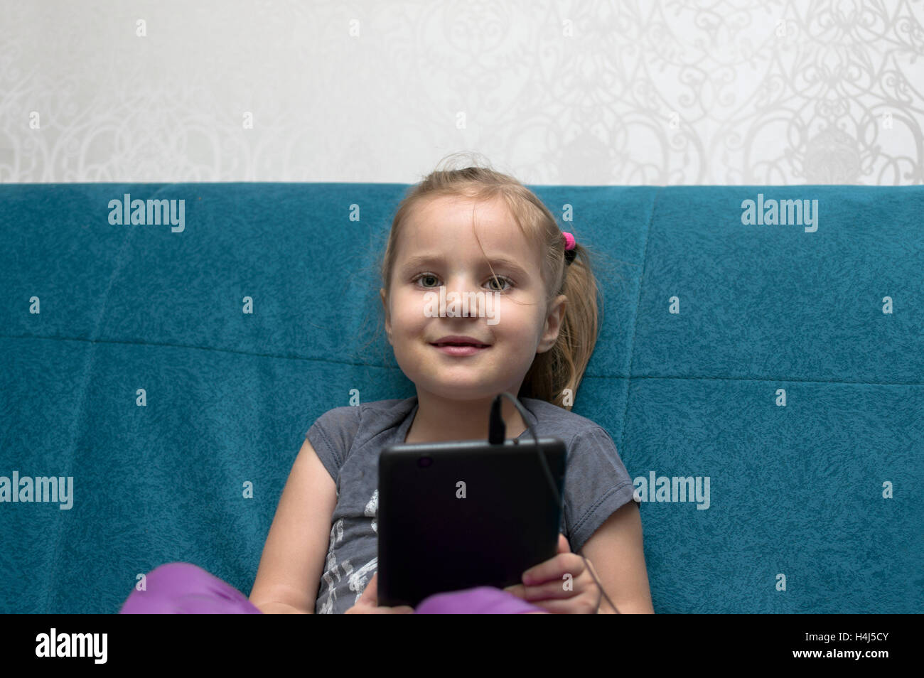A  little girl, looking happy posing with a tablet, sitting on a sofe, indoors cropped portrait Stock Photo
