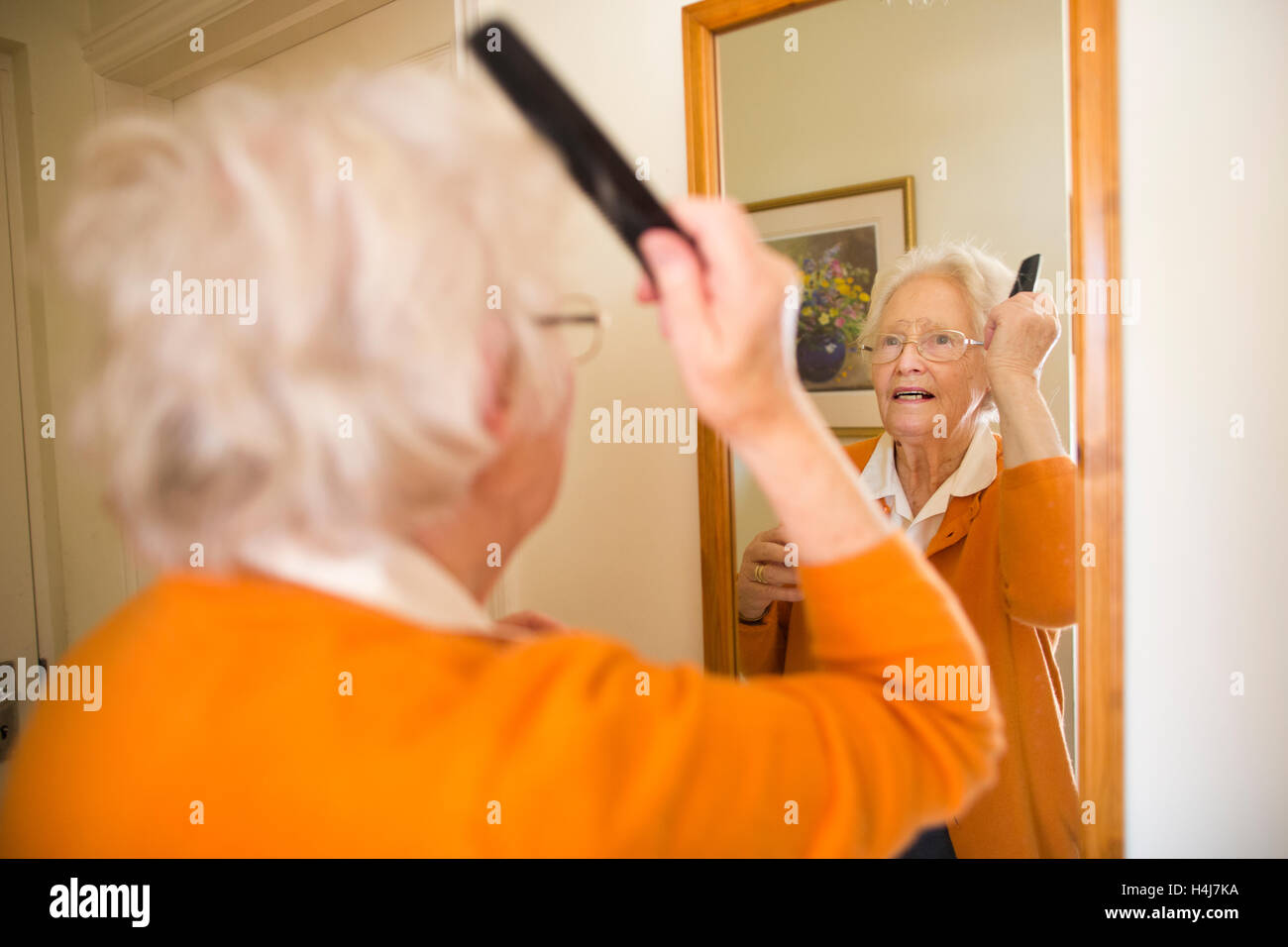 Elderly lady combing her hair in mirror at home, UK Stock Photo