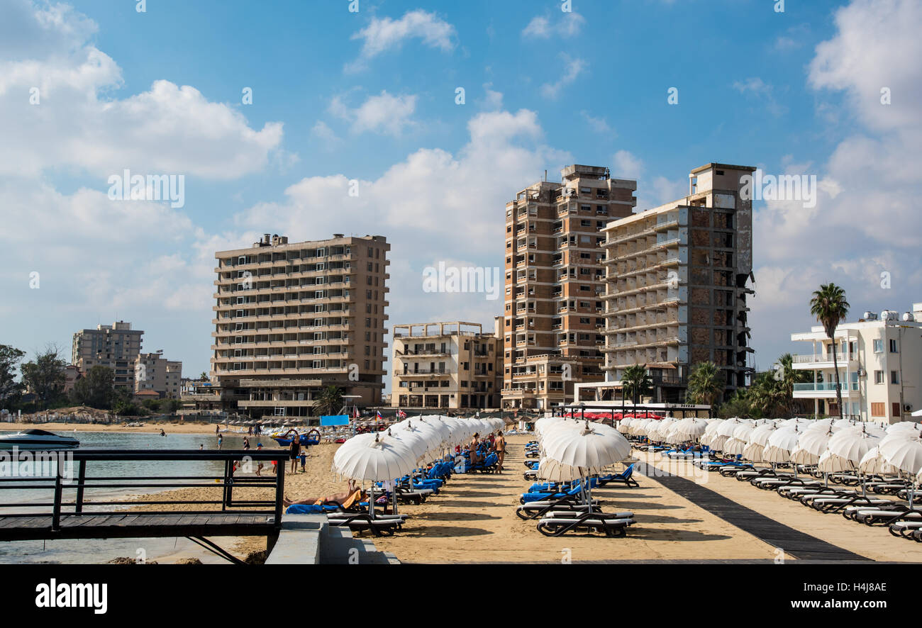 Palm Beach with beach umbrellas and tourists and the abandoned hotels at Varosha ghost town, Famagusta, Northern Cyprus Stock Photo