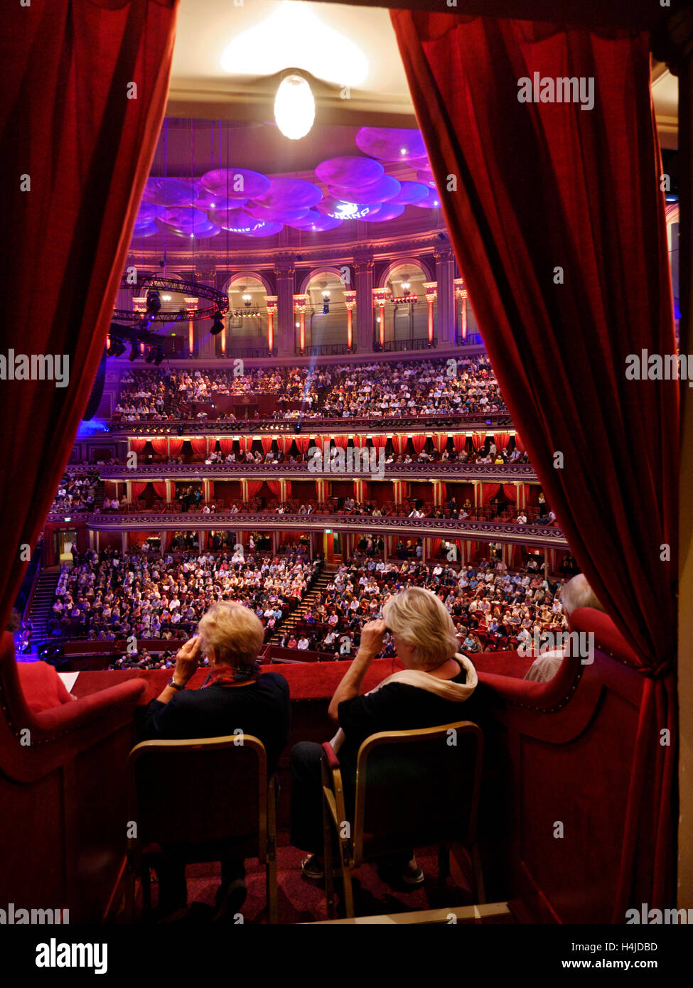Two ladies watching a performance through opera glasses in a plush red