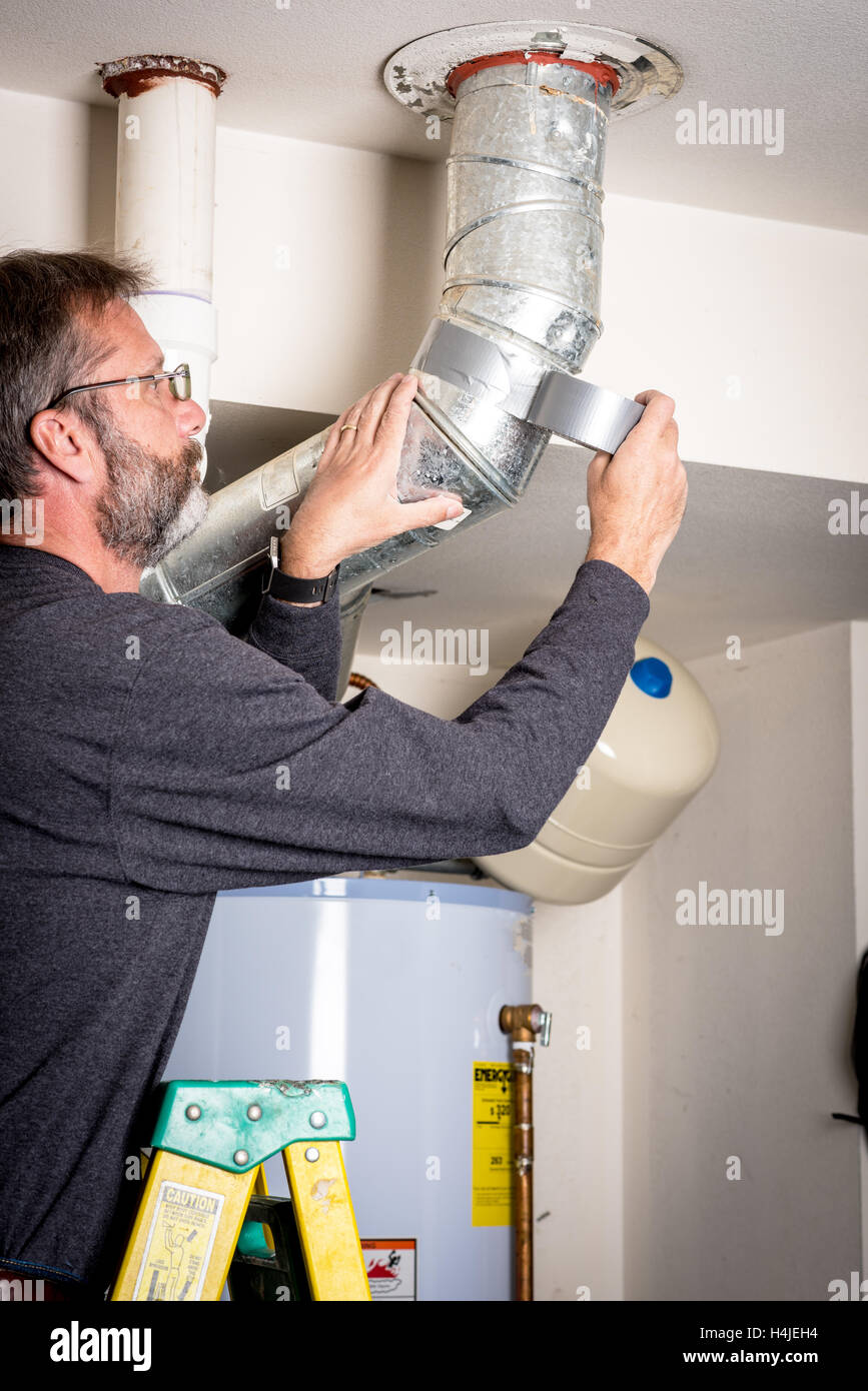 Man applies duct tape to a Hot Water Heater duct Stock Photo