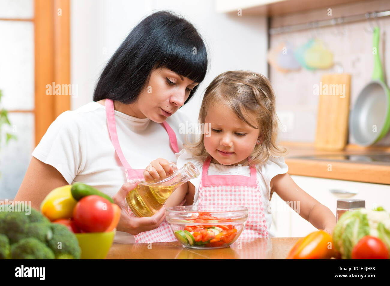 Mother teaching child making salad in kitchen. Cooking concept of happy family preparing food for dinner. Stock Photo