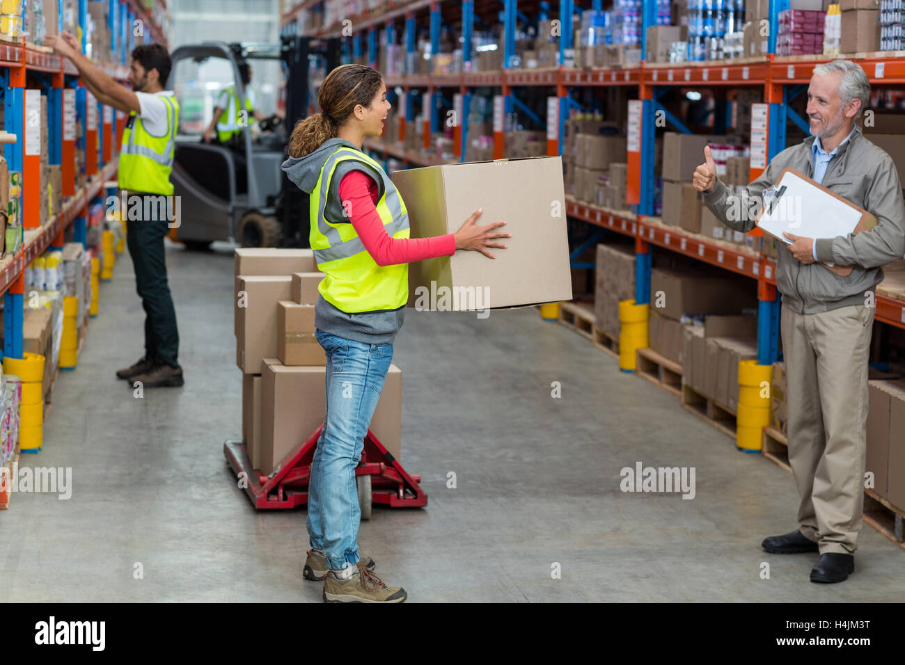 Warehouse manager showing thumbs up to female worker while carrying cardboard boxes Stock Photo