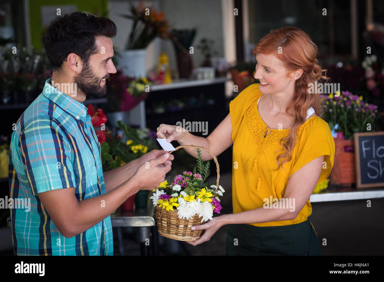 Female florist giving visiting card and flower basket to customer Stock Photo