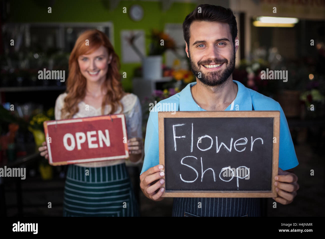 Man holding slate with flower shop sign and woman holding open signboard Stock Photo