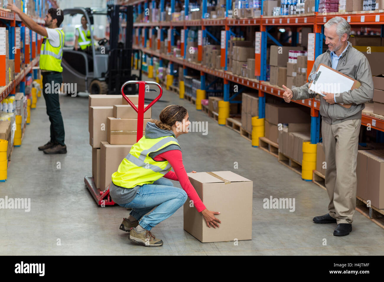 Warehouse manager showing thumbs up to female worker while carrying cardboard boxes Stock Photo