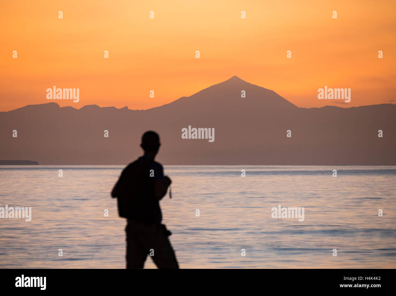 Las Palmas, Gran Canaria, Canary Islands, Spain. 17th October, 2016. Weather: A hiker on Gran Canaria watches the sun set behind Spain`s highest mountain, El Teide (3,718-metres 12,198 ft), more than fifty miles away across the Atlantic Ocean on Tenerife. At 7,500 m (24,600 ft) from its base on the ocean floor, El Teide is also one of the largest volcanos in the world. Credit:  Alan Dawson News/Alamy Live News Stock Photo