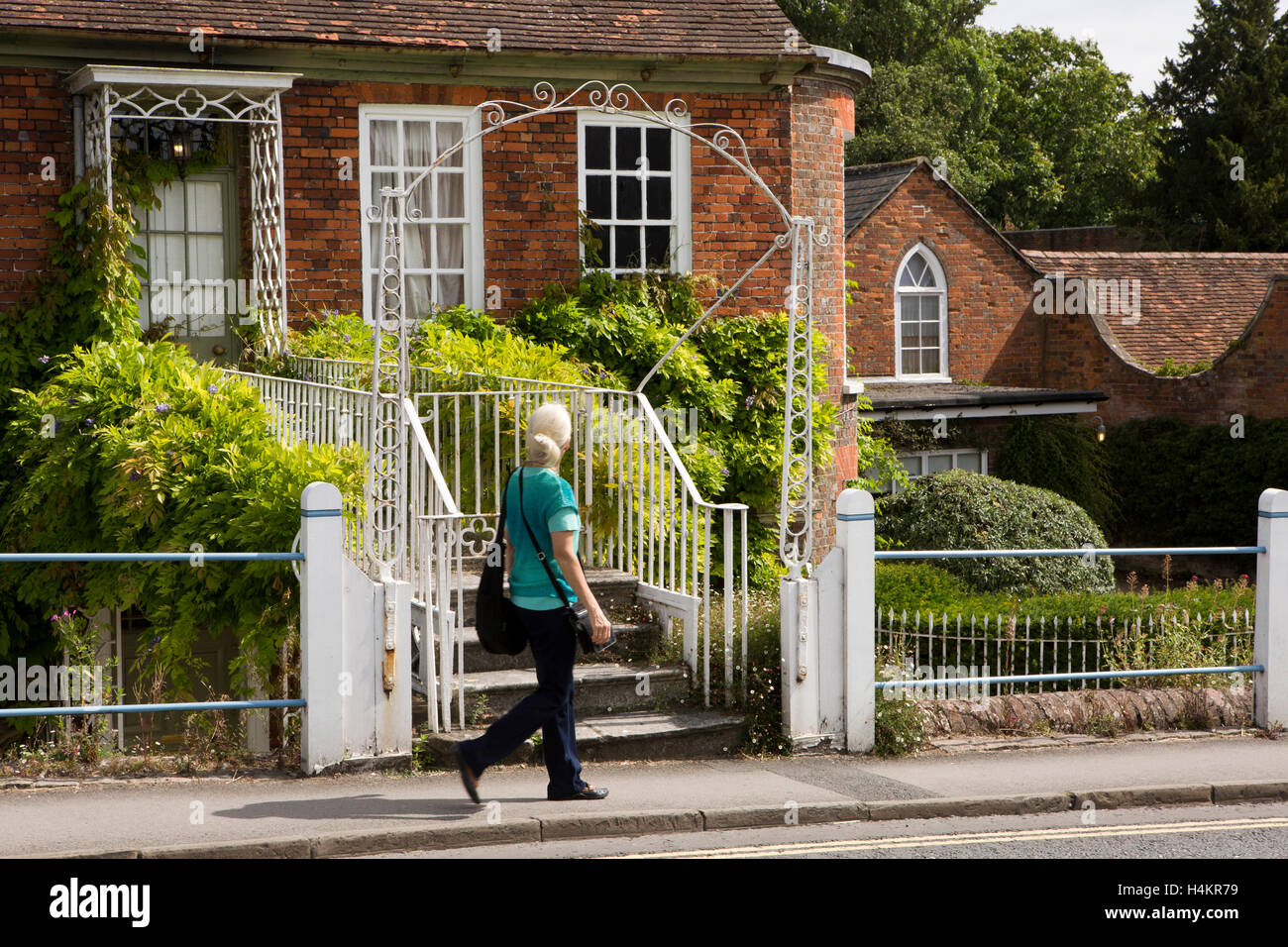 England, Berkshire, Hungerford, High Street, woman walking past house with footbridge to front door beside Kennet and Avon Canal Stock Photo