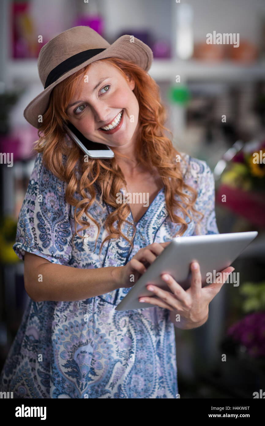 Female florist talking on mobile phone while using digital tablet Stock Photo