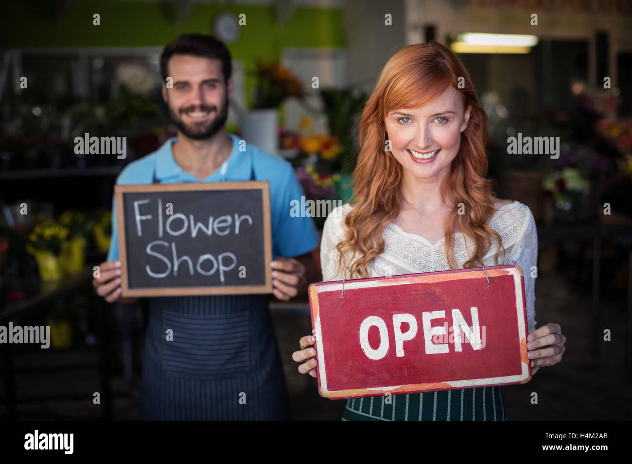 Woman holding open signboard and man holding slate with flower shop sign Stock Photo