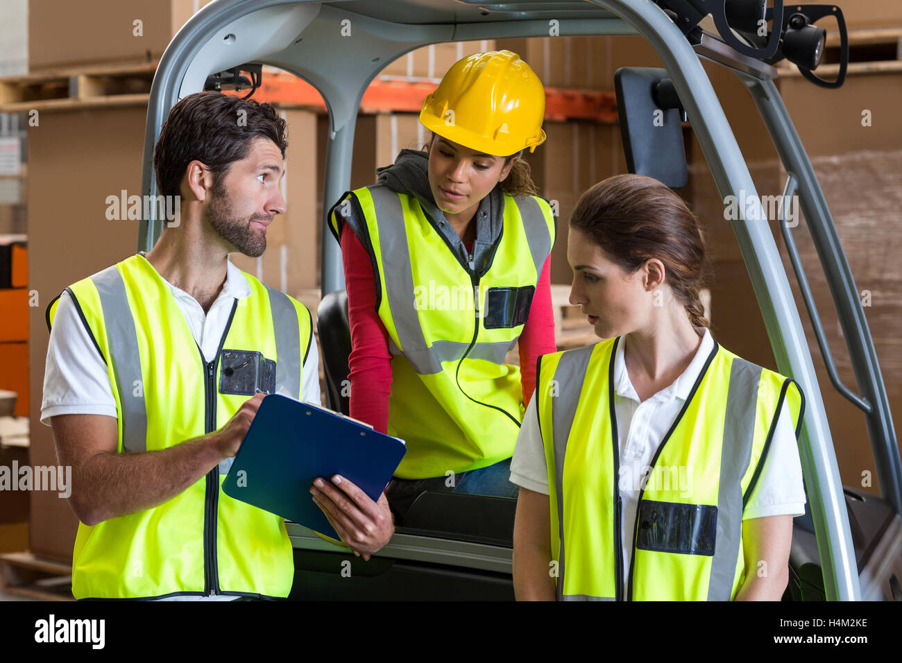 Warehouse workers talking with forklift driver Stock Photo