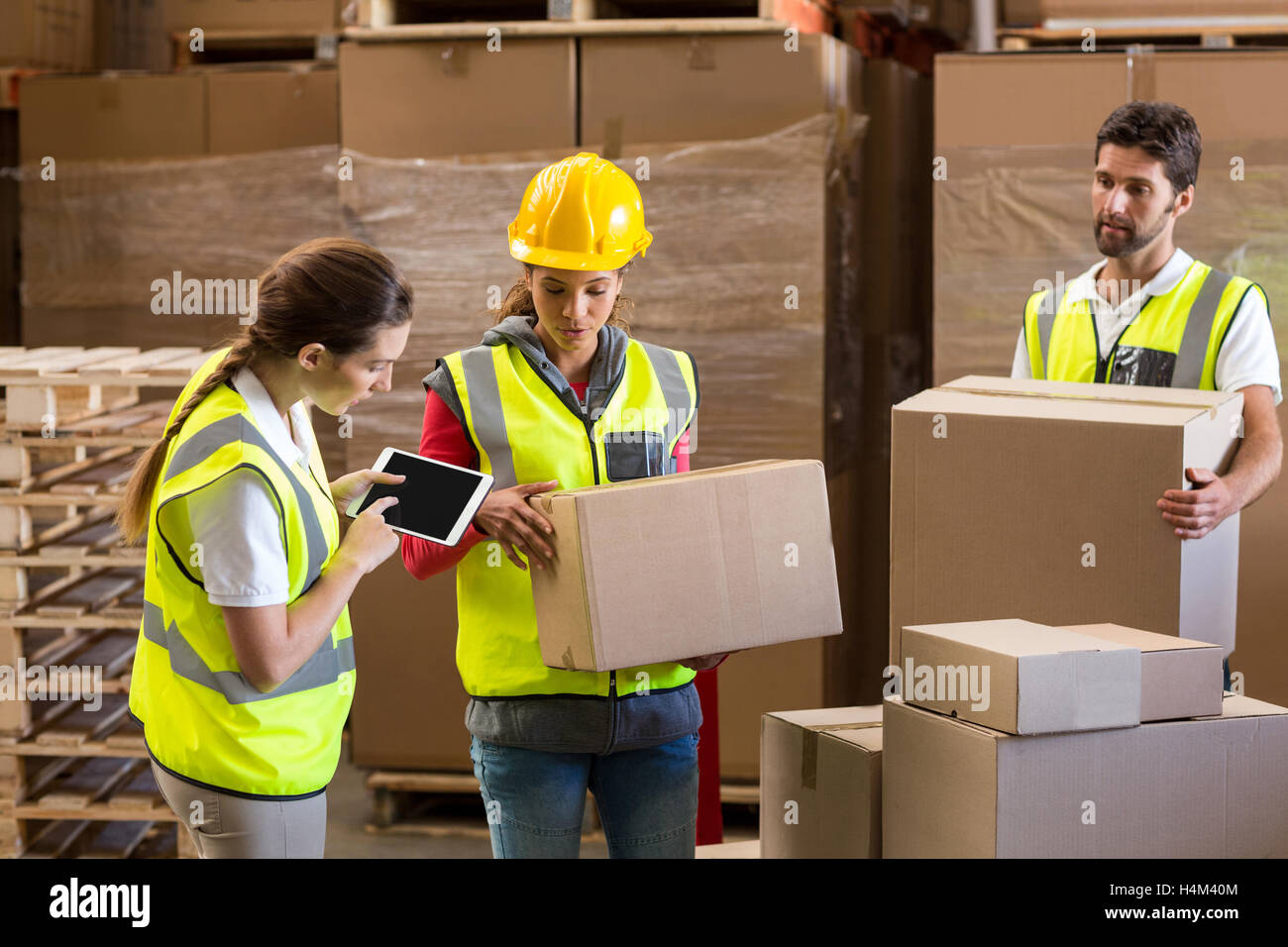 Manager noting on digital tablet while workers carrying cardboard boxes Stock Photo
