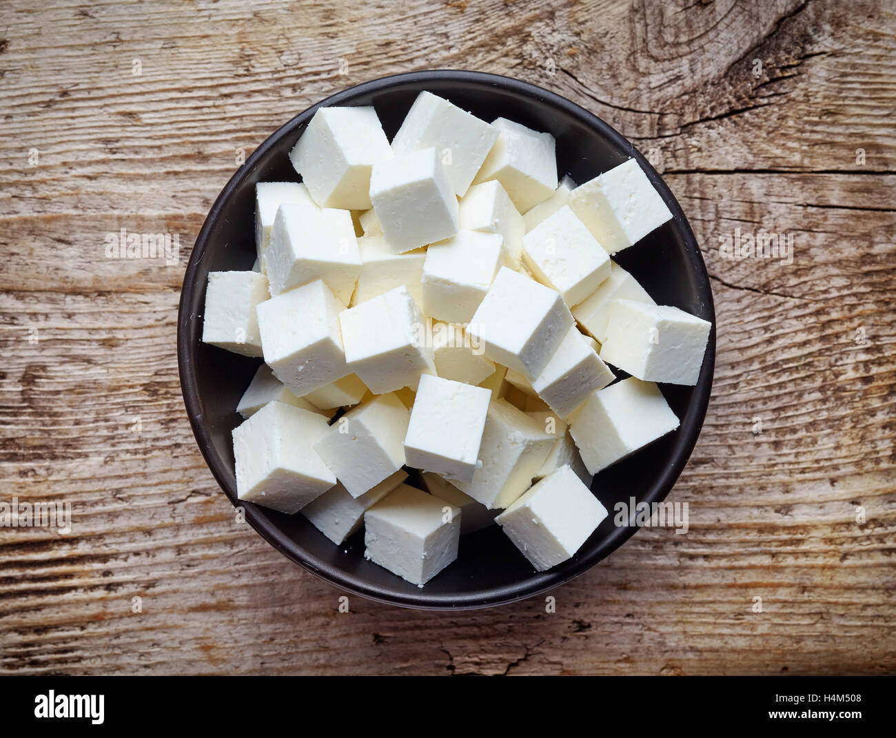 Bowl of diced soft cheese on wooden background, top view Stock Photo