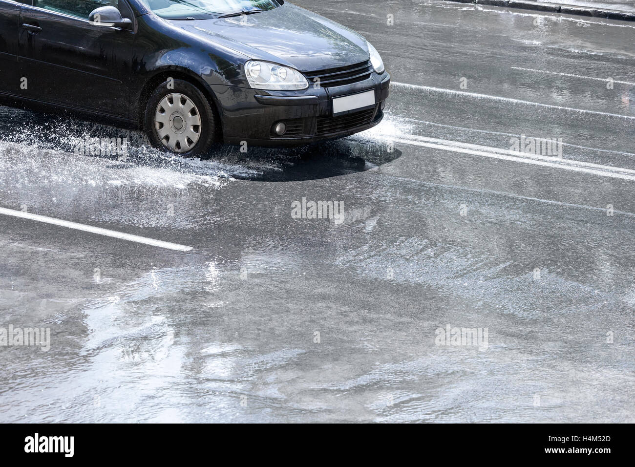black car driving through water puddles on city street after rain under