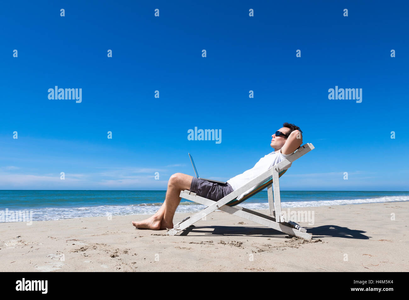 Freelancer working remotely with laptop and resting on sunny tropical beach, sunglasses Stock Photo