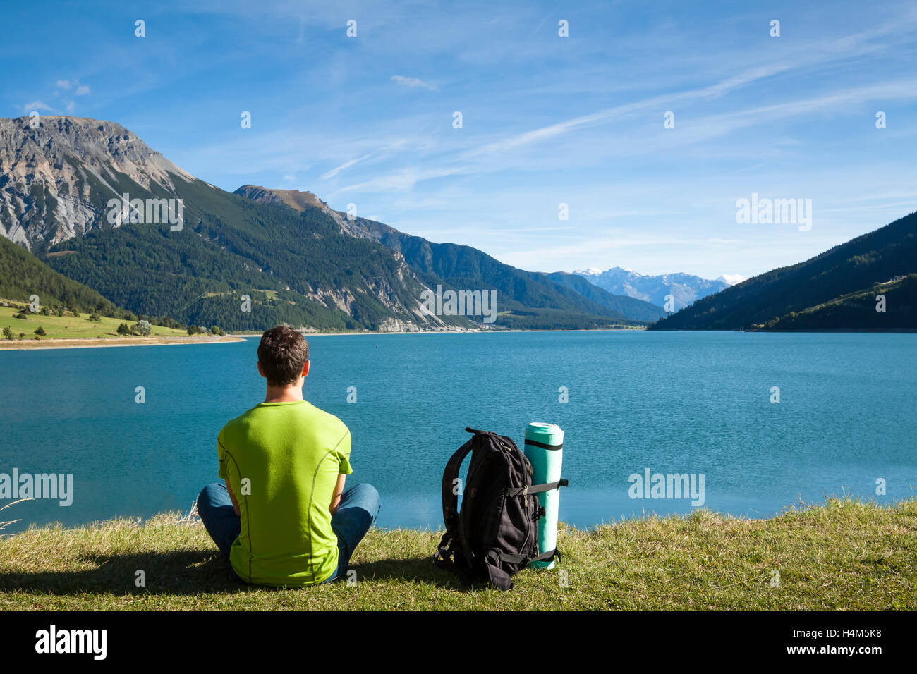 Hiker with backpack and rolled foam camping mattress looking at the lake with mountain background Stock Photo