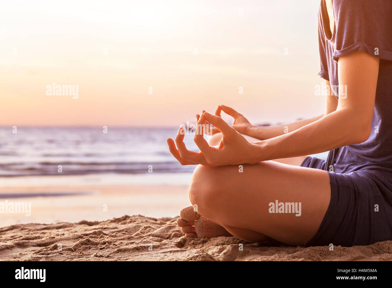 Young woman practicing yoga on the beach for harmony, close-up of hands, gyan mudra and lotus position Stock Photo