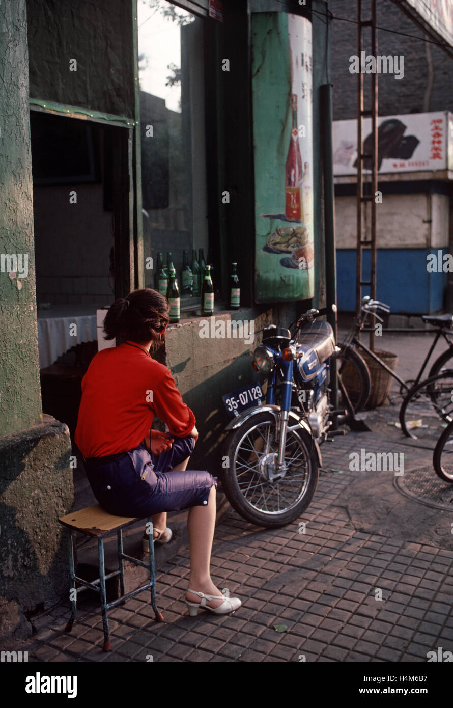 Chinese woman sitting in front of restaurant bar with food and drink painted advertising sign in Harbin, Heilongjiang Province, China Stock Photo