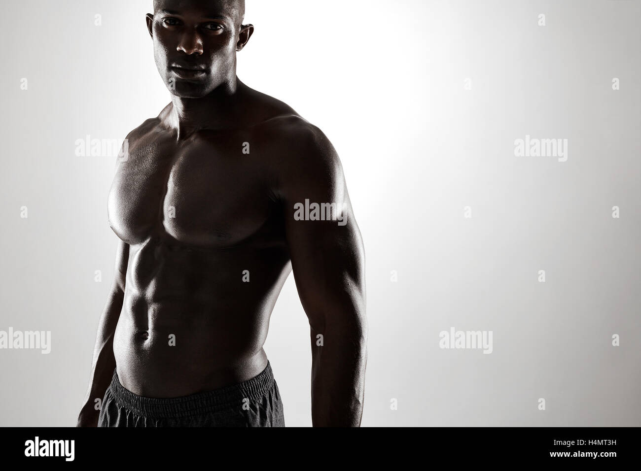 Portrait of young afro american man with muscular physique. Shirtless male model standing confidently against grey background. Stock Photo