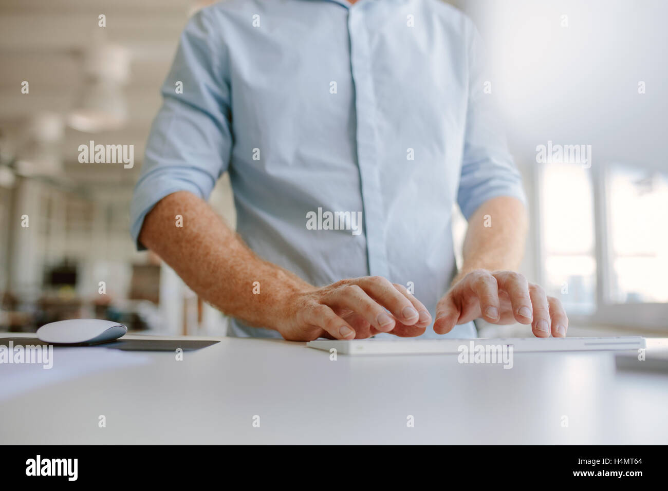 Close up of businessman hands typing on computer keyboard. Cropped shot young man working on computer while standing at his desk Stock Photo