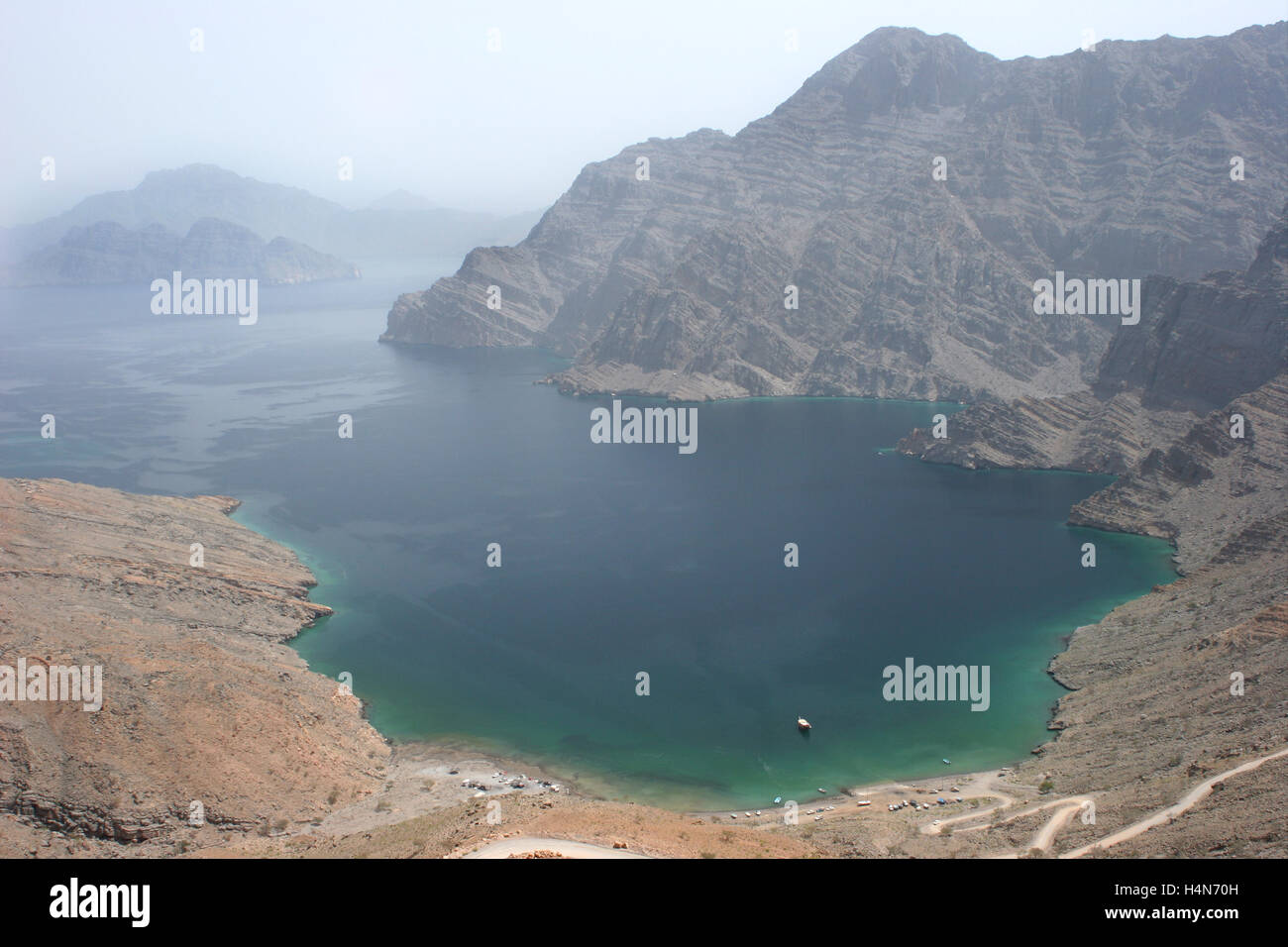 The wild landscape of the Musandam Peninsular at Khor an Najd in northern Oman.  A single dhow is moored in the bay Stock Photo