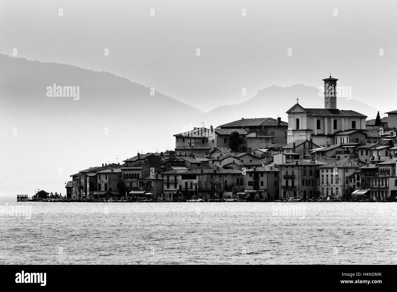 Distant small fishing village on lake como waterfront in Italy facing calm water with alps mountains in the background. Stock Photo