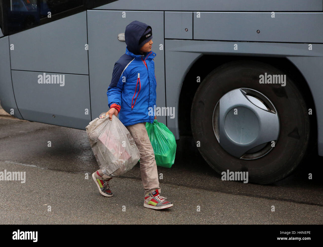 A young boy carries his belongings as families prepare to board a coach at the jungle migrant camp in Calais, France, to start a new life in southern France as plans are made to demolish the camp over the next few weeks. Stock Photo