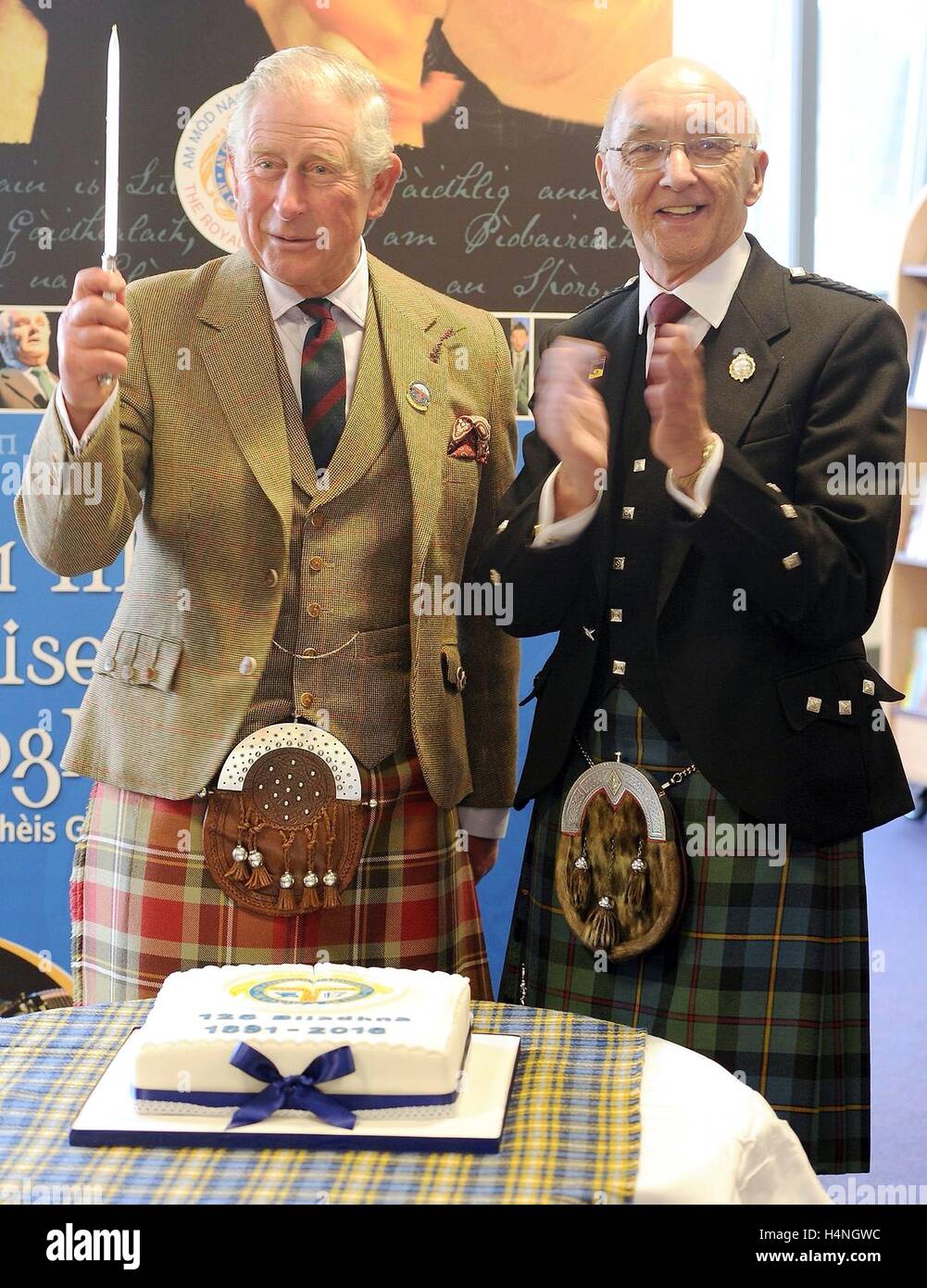 The Prince of Wales, known as the Lord of the Isles while in the Western Isles, (left) cuts a commemorative cake to mark the 125th anniversary of An Comunn Gaidhealach, alongside John Macleod, President of An Comunn Gaidhealach, at the Nicholson Institute in Stornoway, Isle of Lewis. Stock Photo