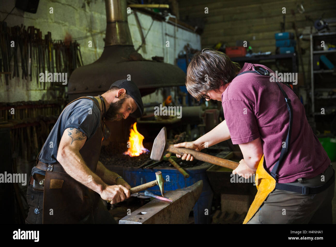 Two blacksmiths hammer a piece of metal on anvil in a workshop Stock Photo