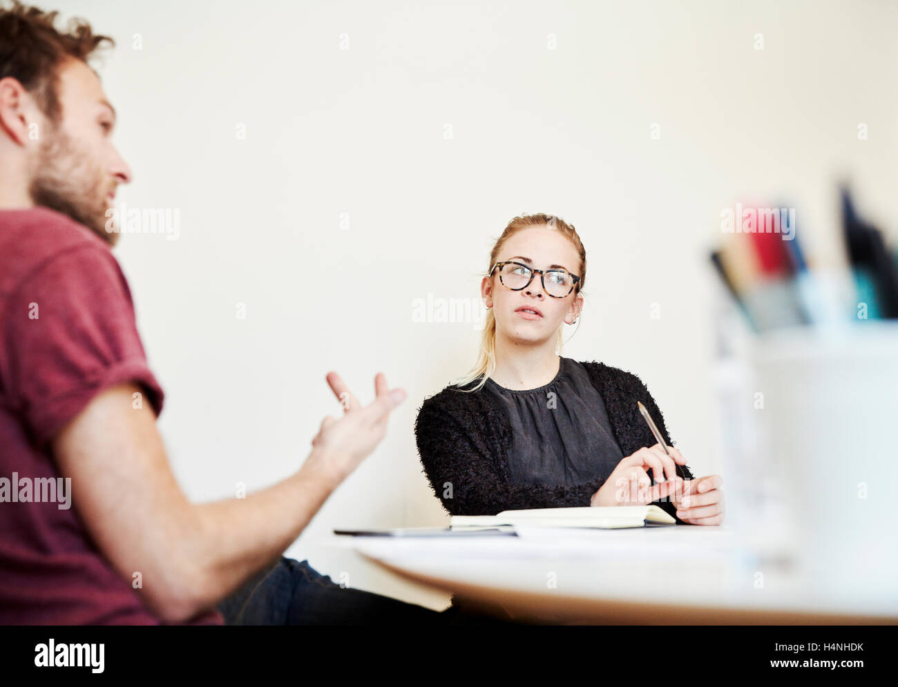 Two people at a meeting, a man gesticulating and a woman listening. Stock Photo