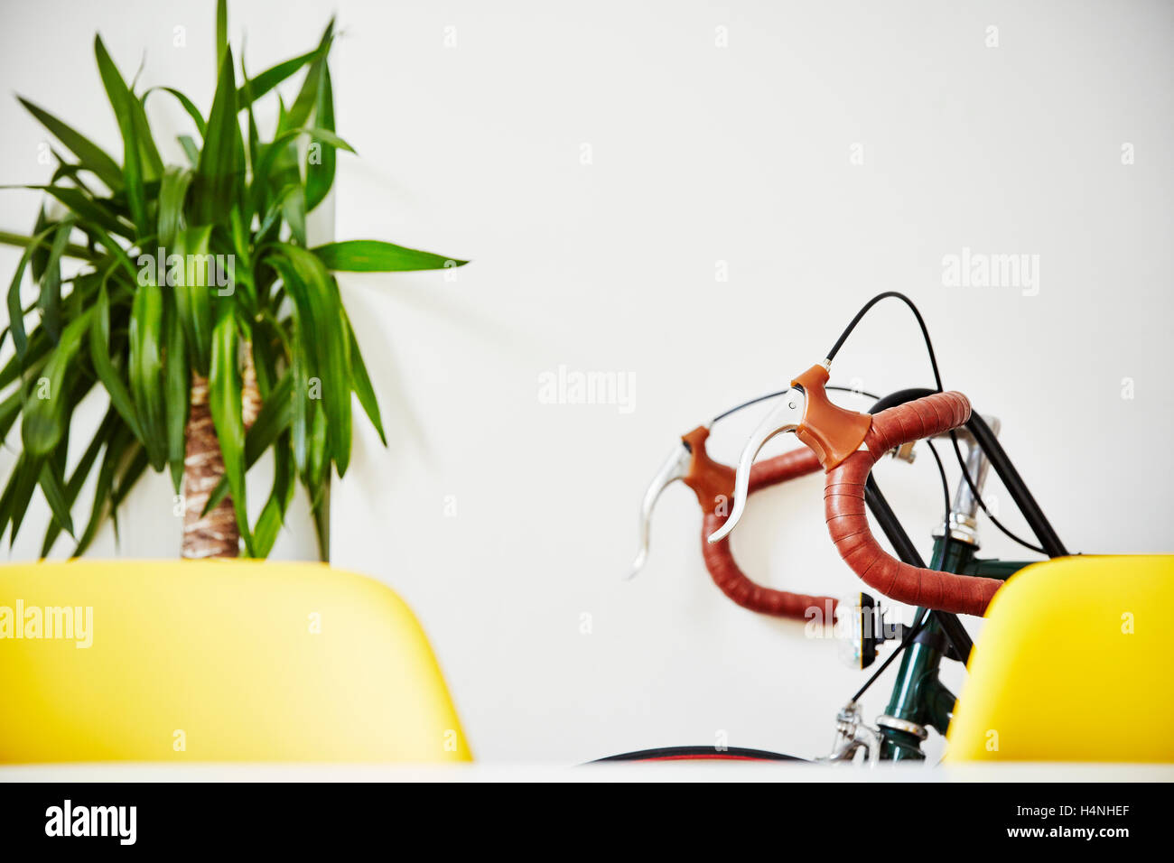 A bicycle with red curved handle bars leaning against a white wall, beside a plant. Stock Photo