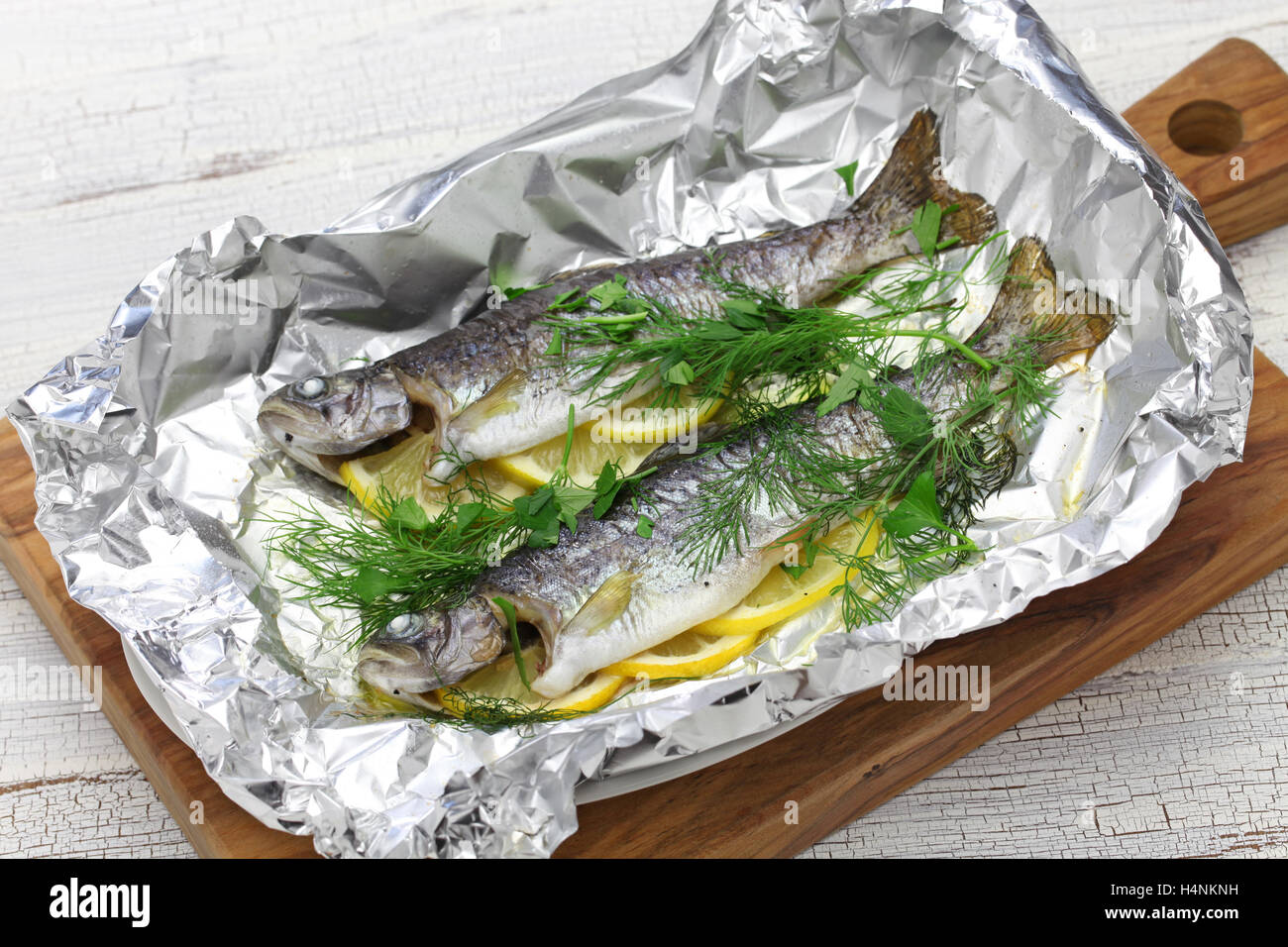 whole rainbow trout baked in foil on cutting board Stock Photo