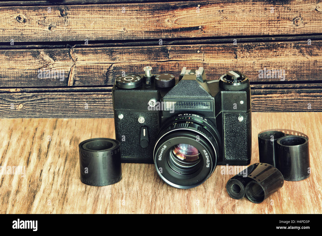 Old retro photo camera and film negative strip on wooden table against timber wall.Toned image. Stock Photo