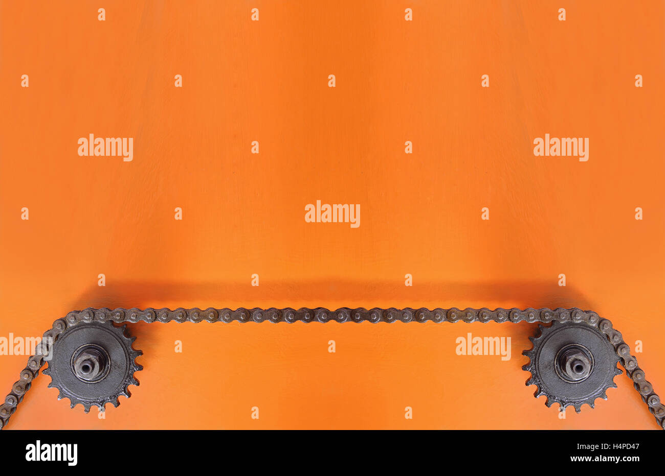 Black metal cogwheels and chain on orange background with empty space. Stock Photo