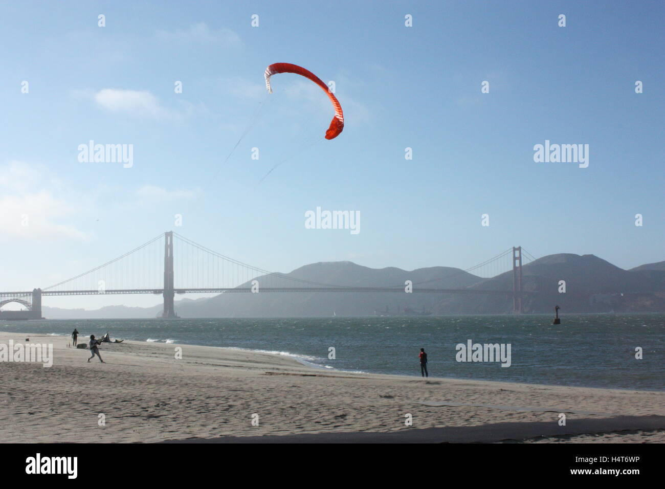 The Golden Gate Bridge with someone flying a kite on the beach next to the sea Stock Photo
