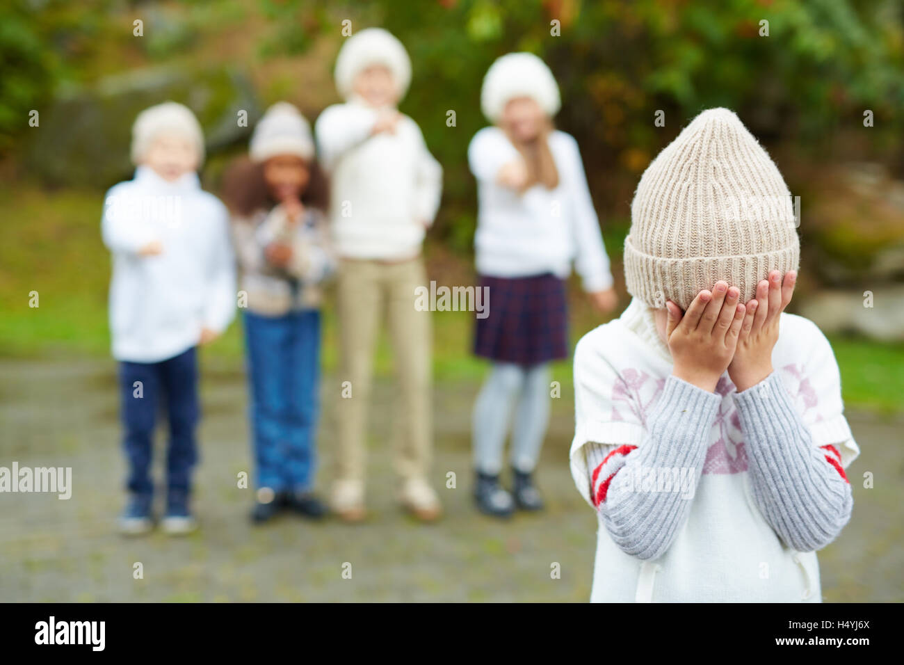 Little boy crying with his face in hands on background of bullying children Stock Photo