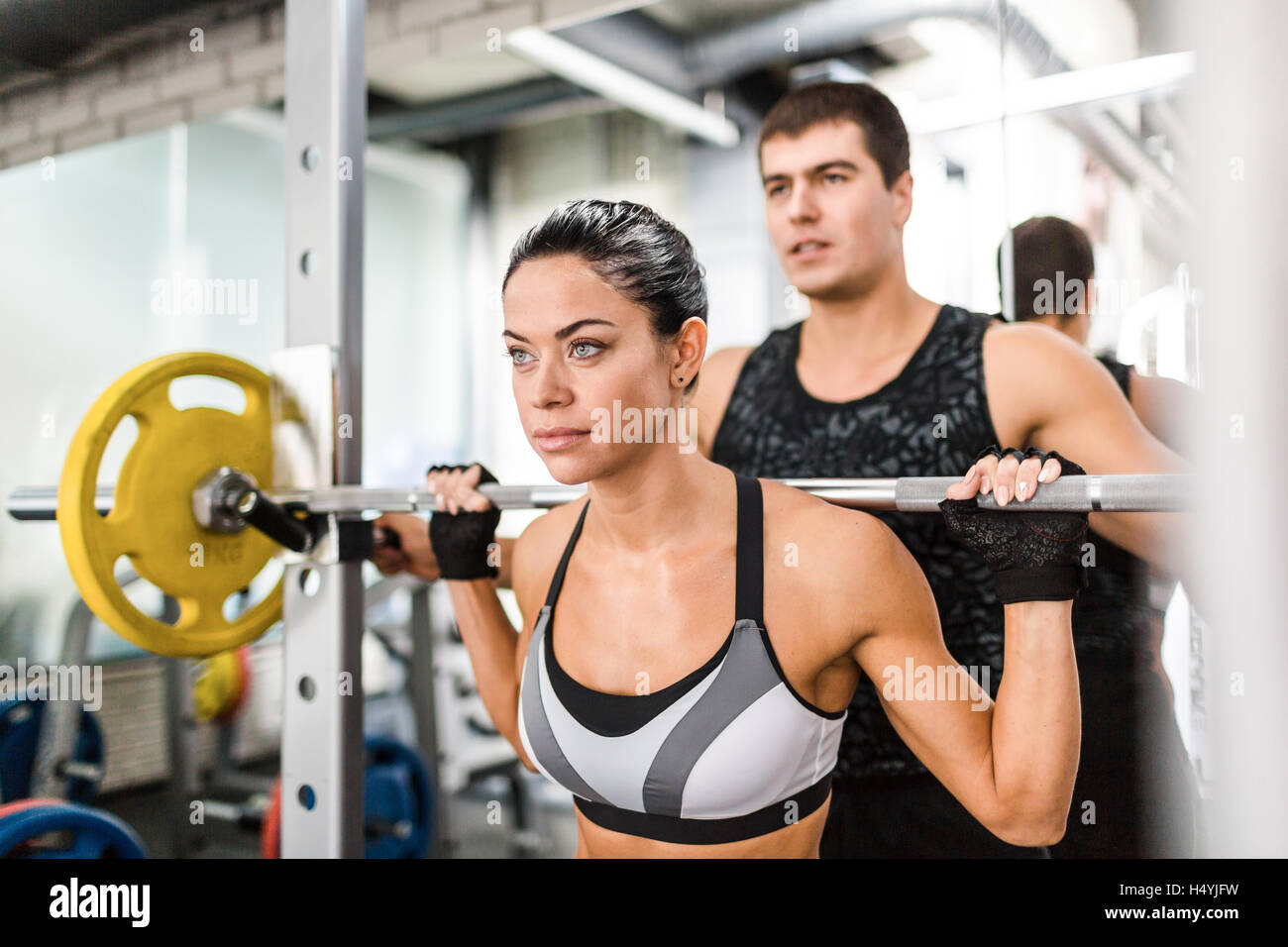 Sweating woman lifting weight in gym with help of her trainer Stock