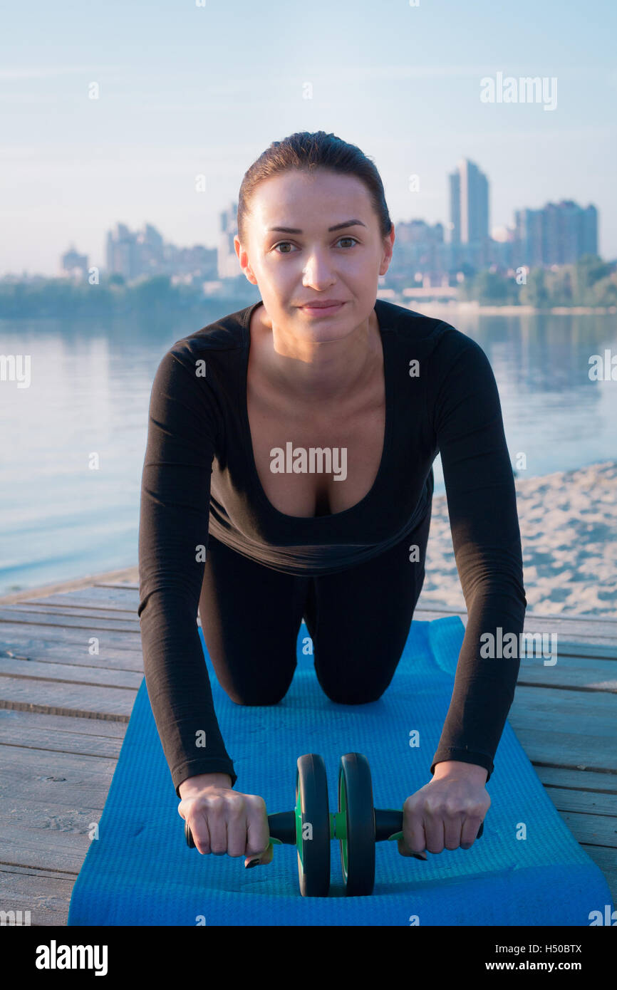 Young pretty fitness woman exercises on pier during morning sport training workout Stock Photo