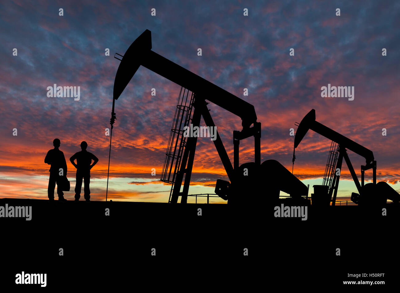 Silhouette of oil workers at an oil field pumpjack site against a dramatic sky. Stock Photo